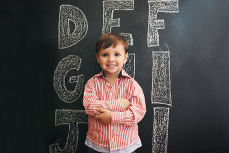 Learning the ABCs. A little boy standing in front of a blackboard with letters written on it.の写真素材