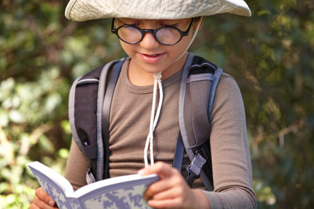 Reading and nature are his two favourite things. a young kid reading a book outdoors.の写真素材