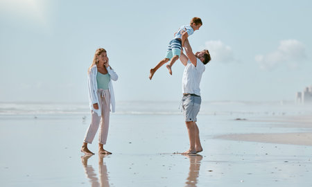 Family, beach and father lifting kid on vacation, holiday or summer trip outdoors. Love, support and care of mother, man and boy playing, bonding and having fun while enjoying quality time togetherの写真素材