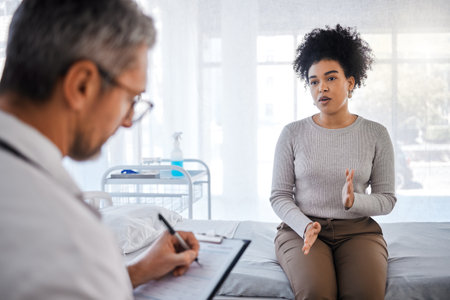 Healthcare, consulting and insurance with a black woman patient sitting in a hospital with her doctor. Medical, consultant and insurance with a female talking to a medicine professional for diagnosisの写真素材