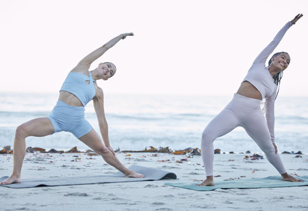 Yoga, women and stretching on beach in the morning, balance and fitness for wellness, health or peace outdoor. Young females, girls and meditation for breathing, relax and workout for zen on seaside.の写真素材