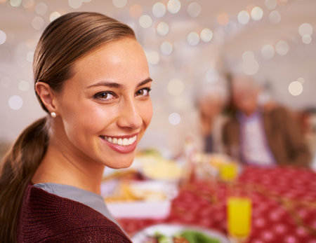 Good food and great family moments. A young woman smiling at the christmas table with her family in the background.の写真素材