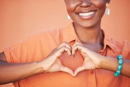 Heart, love and black woman hands for beauty, african self care and fashion cosmetics with peace, happiness and smile with teeth. Summer, orange wall background and happy woman with self love signの写真素材