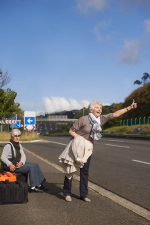 Making their escape from the retirement village...Two senior ladies hitch-hiking by the side of the road.の写真素材
