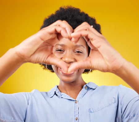 Love, heart hands sign and portrait of black woman, smile and kindness isolated on yellow background. Motivation, support and loving hand gesture, happy African model in studio with caring mindset.の写真素材