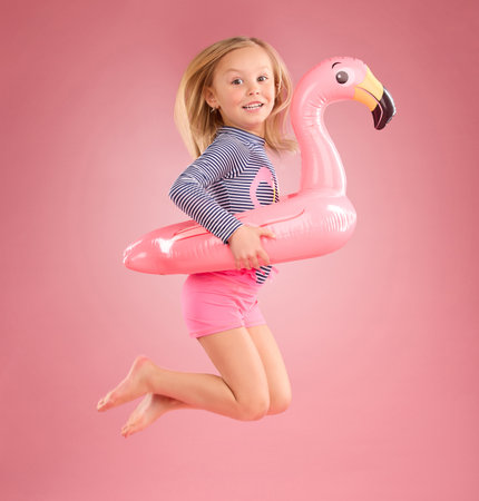 Jump, smile and portrait of girl and pool float for swimming, summer break or happiness. Youth, funny and inflatable with child and flamingo ring for cute, happy or beach holiday on pink backgroundの写真素材