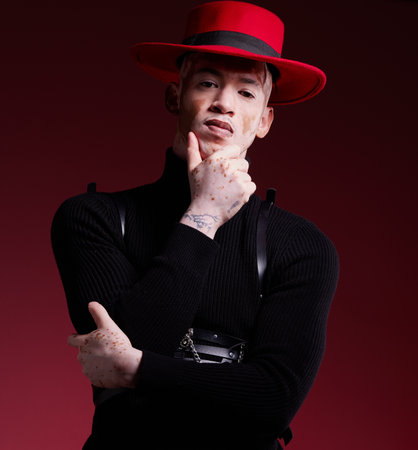 Man, fashion style or vitiligo skin on red background studio in empowerment, self love or attitude. Portrait, aesthetic or model with cool, stylish or edgy clothes or South Africa facial pigmentationの写真素材
