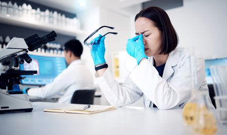 Headache, science and research with a woman at work in a laboratory with anxiety or suffering burnout. Doctor, stress and medicine with a female scientist working in a lab with mental health issuesの写真素材