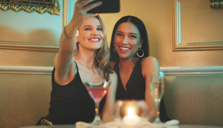 Girl friends, phone and selfie at a nightclub for cocktail celebration with happy women and alcohol. Mobile photo, smile and restaurant drinks of people at a event for new year or happy hourの写真素材