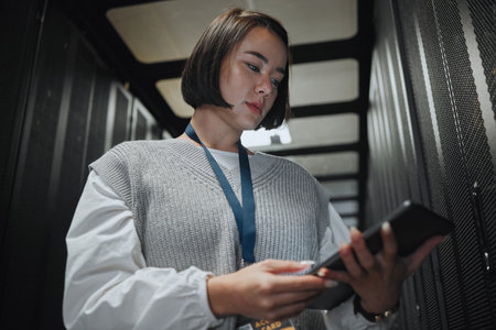 Server room, phone and engineering on cybersecurity mobile app, programming software or safety check. Network, smartphone and asian person, technician or programmer with data center or power analysisの写真素材