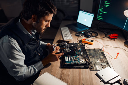 Night, technician and working on motherboard repair overtime and manufacturing an electronic device in a workshop or shop. Person, man and guy fixing hardware of a computer for technology in a labの写真素材