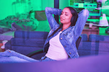 Woman, headphones or relax in neon house after technology coding, software development or cybersecurity safety. Happy, programmer or hands behind head in night programming success with music podcastの写真素材