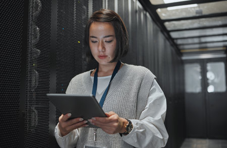 Tablet, server room and security with a programmer asian woman at work on a computer mainframe. Software, database and information technology with a female coder working alone on a cyber networkの写真素材