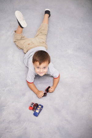 Playing in the garage. High angle shot of a cute young boy playing with toy cars.の写真素材
