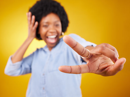 Happy, peace sign and hand of a black woman in studio with a positive and goofy mindset. African female model posing with finger gesture while happy about motivation or victory on yellow backgroundの写真素材