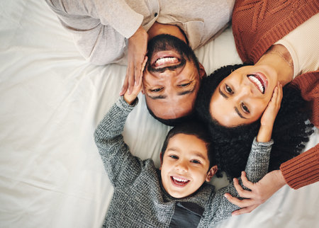 Top view, love and family in bedroom, smile and quality time for joy, bonding and happiness. Portrait, parents and mother with father, boy and male child on bed, cheerful and relax with affectionの写真素材