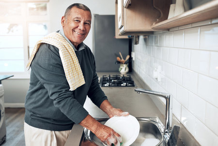 Cleaning, washing dishes or portrait of happy old man with soap water in kitchen sink in healthy home. Dirty, smile or senior male with liquid foam to disinfect, protect or prevent bacteria or germsの写真素材