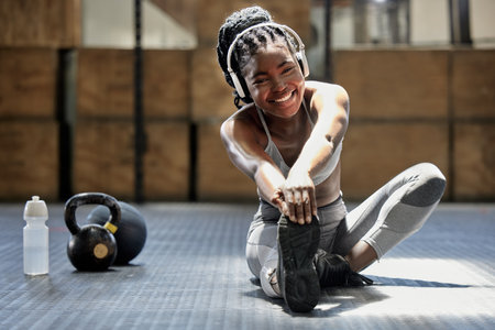 Portrait of woman stretching with music at gym, audio podcast for workout motivation and happy about fitness training on floor at health club. African athlete or sports person doing exerciseの写真素材