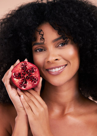 Face, hair care and portrait of black woman with pomegranate in studio isolated on a brown background. Fruit, skincare and happy female model holding food for healthy diet, nutrition and vitamin c.の写真素材
