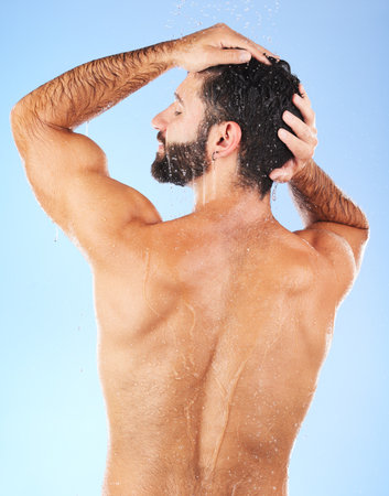 Water, shower and back of man in studio for skincare, wellness and shampoo cosmetics on blue background. Hair, body and male model cleaning with water, beauty and dermatology on bathroom backdropの写真素材