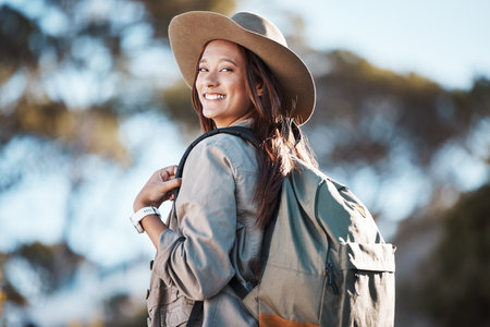 Hiking, portrait and woman in nature for freedom, travel and backpacking adventure on blurred background. Face, girl and traveler walking in a forest, smile and excited for journey, vacation or tripの写真素材