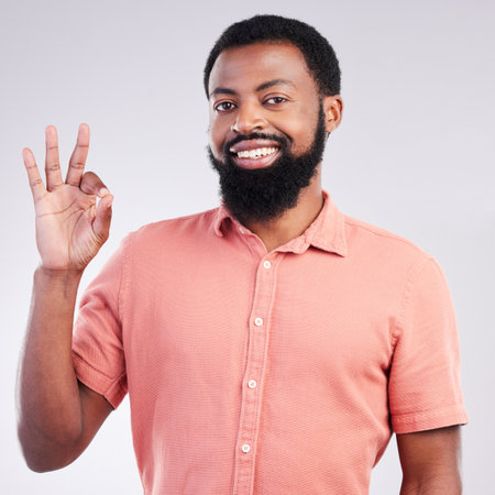 Portrait, perfect and hand gesture with a black man in studio on a gray background to say magnifique. Emoji, communication and okay with a happy or handsome young male speaking in sign languageの写真素材