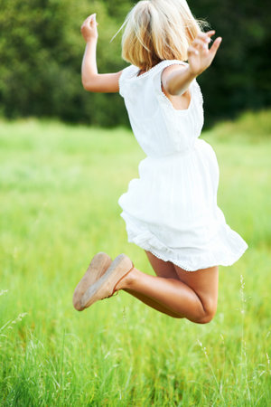 I feel great. Beautiful young woman jumping while in a field outdoors.の写真素材