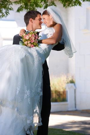 Theyre a support to each other. a groom playfully carrying his new bride outside.の写真素材
