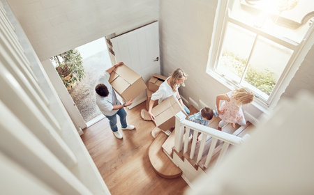 Above view happy caucasian family moving into their new home and carrying boxes up a staircase. Parents and kids moving in. Mother, father, brother and sister taking their belongings into a new houseの写真素材