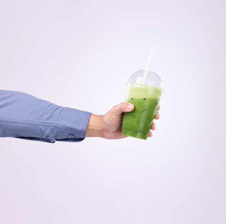 Green juice in man hands isolated on a white background diet, detox and healthy breakfast or protein drink offer. Person or nutritionist hand holding or giving smoothie for vegan choice in studioの写真素材