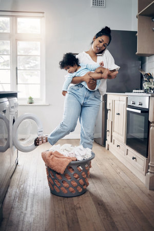 Busy day for this working mom. a young mother using a cellphone while completing housework and holding her baby at home.の写真素材