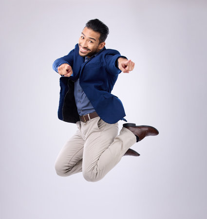 Jump, excited and portrait of man point in studio with surprise, happiness and celebration on white background. Winner, success mockup and isolated happy male jumping with energy, smile and victoryの写真素材