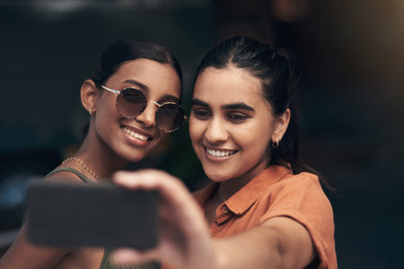 This was a day to remember. two young friends standing outside a restaurant and using a cellphone to take a selfie.の写真素材