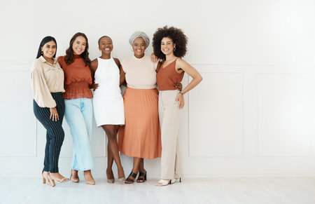 Group of five young happy cheerful businesswomen embracing while standing against a wall in an office. Portrait of diverse happy colleagues smiling standing in a line at work togetherの写真素材