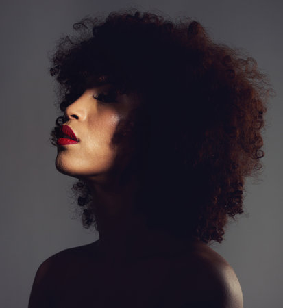 Beauty, shadow and woman with afro and makeup as skincare, cosmetic and self care in the dark or night. Spotlight, creative and face of female model with mystery aesthetic and luxury fashionの写真素材
