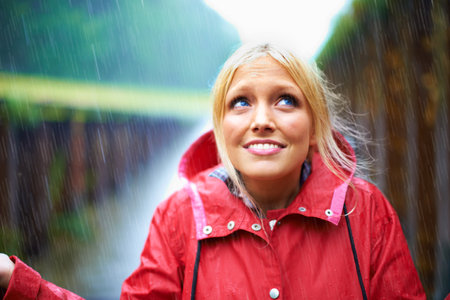 Its started raining. Gorgeous young blonde woman wearing a red raincoat in the rain outdoors on a country road.の写真素材