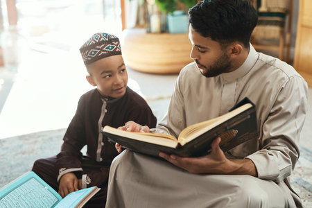 To take children seriously is to value them. a young muslim man and his son reading in the lounge at home.の写真素材