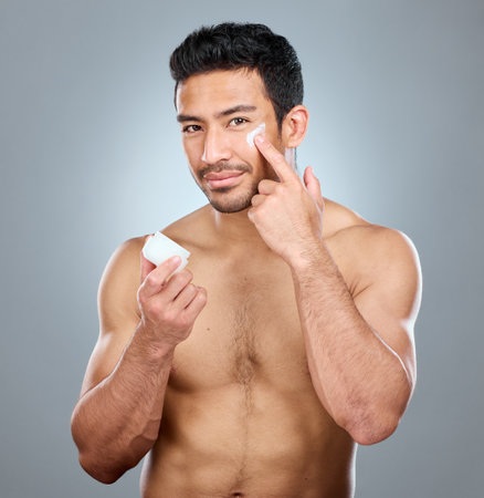Ill show you what this product does for me. a man applying moisturiser to his face while standing against a grey background.の写真素材