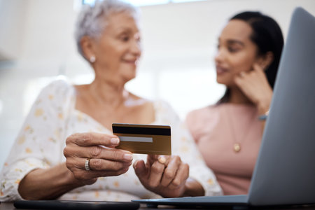 Back in the day we paid bills at the bank. a senior woman using a laptop and credit card with her daughter at home.の写真素材