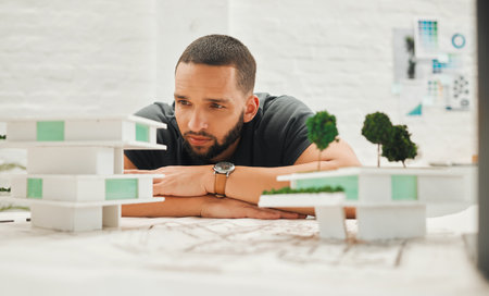 Focused architect looking at building model. Young businessman thinking about a building model. Handsome engineer working on a 3D building model. Engineer working on a 3D modelの写真素材