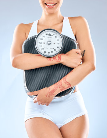The scale became my friend. an unrecognizable woman holding a weighing scale against a grey background.の写真素材