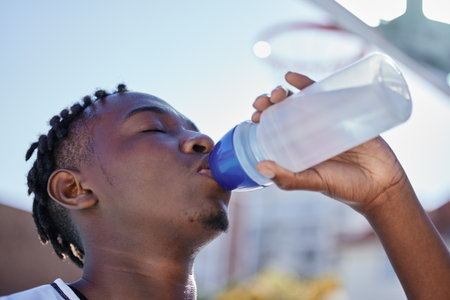 Water, hydration and healthy lifestyle of a sporty black man drinking water from a bottle, enjoying a refreshing drink. African athlete restore electrolytes while being active and exercise outsideの写真素材