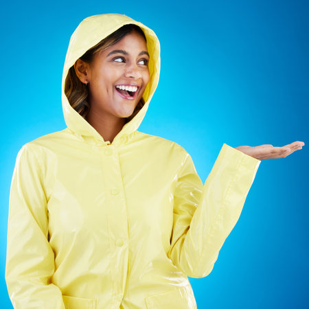 Hand, rain and happy woman in studio excited for weather, drop or storm while posing on gradient blue background. Smile feeling and girl enjoy rainfall, splash and winter season, cheerful or isolatedの写真素材