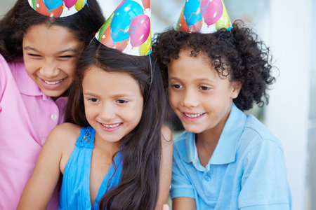 Enjoying her birthday. Three kids wearing party hats at a party.の写真素材