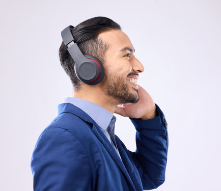 Business, happy man and thinking with music headphones, studio or background of happiness. Smile, young worker and listening to radio, sound and corporate podcast of audio, motivation and inspirationの写真素材