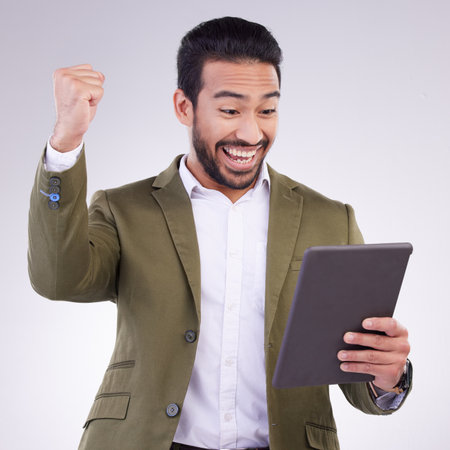 Success, winning and man on tablet isolated on studio background fist pump for business news or online bonus. Happy asian person or winner on digital tech with celebration for sale, prize or giveawayの写真素材