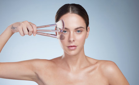 The correct brush makes all the difference. Studio portrait of an attractive young woman posing with a variety of makeup brushes against a grey background.の写真素材