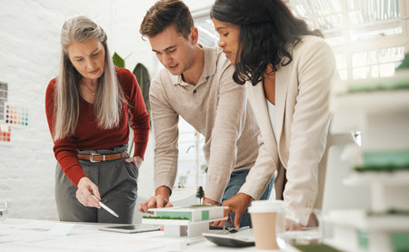 Mature businesswoman talking to staff about blueprint. Senior boss collaborates with staff on...