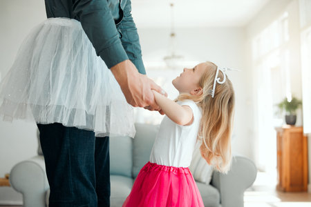 Teaching Daddy how to dance. an adorable little girl wearing a tutu and dancing with her father in the living room.の写真素材