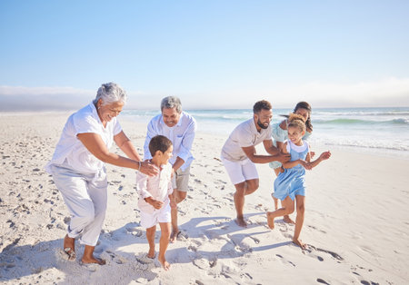 Children being chased by their parents and grandparents on the beach. Carefree mixed race family having fun by the sea while on vacationの写真素材